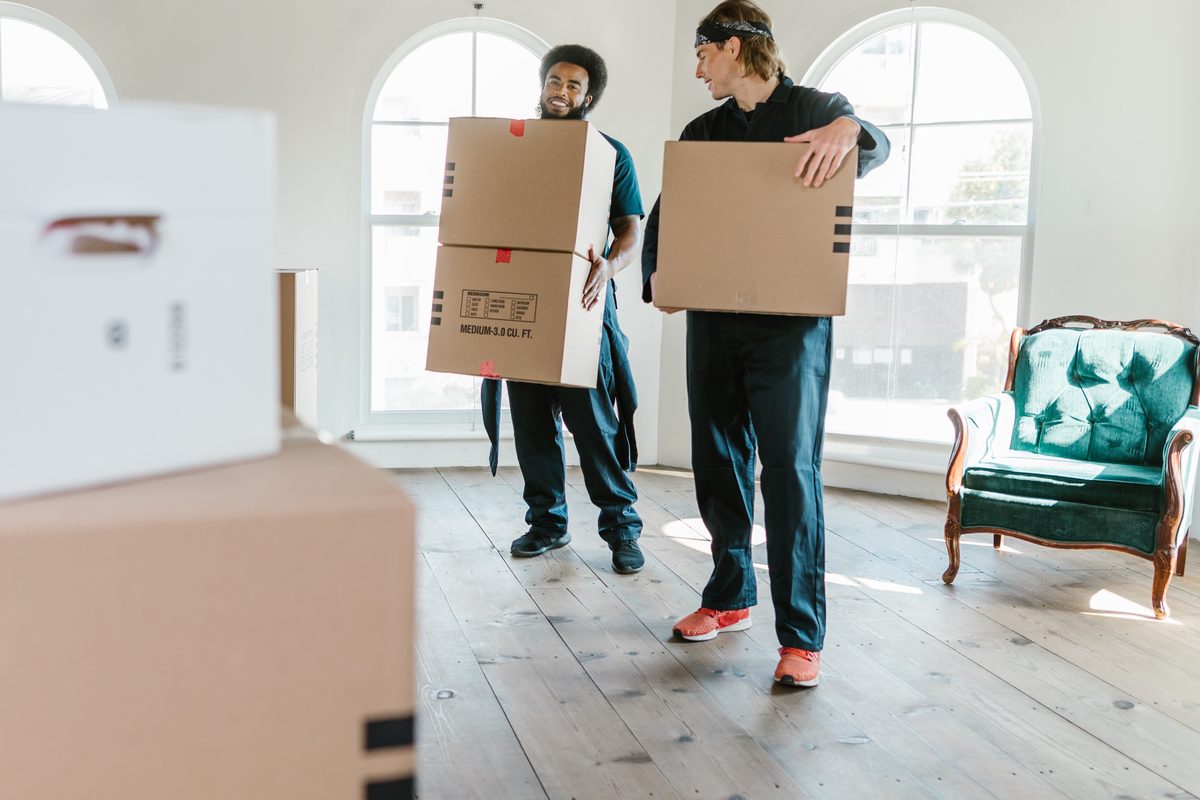 Deux professionnels en tenue de travail portant des cartons dans un logement en cours de vidage