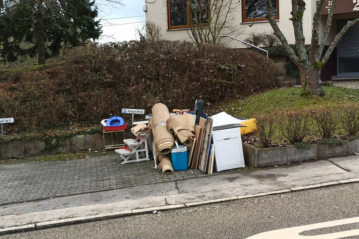 Encombrants déposés en bordure de trottoir devant une maison : tapis roulés, petit meuble, étagères et glacière